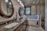 The ensuite bathroom has a step in glass shower, a dual vanity with granite countertops and a lush soaking bathtub